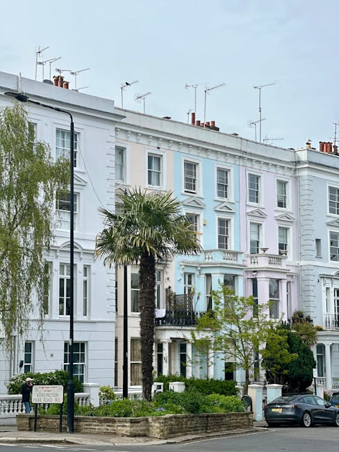 A row of elegant white Victorian-style terraced houses in Notting Hill, featuring large sash windows, decorative cornices, and small balconies. In the foreground, a landscaped sidewalk includes a tall