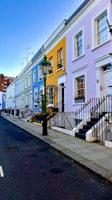 The image features a row of traditional terraced houses on a quiet street in Notting Hill, featuring vibrant pastel facades in shades of light blue, yellow, lavender, and white. Each house has white-f