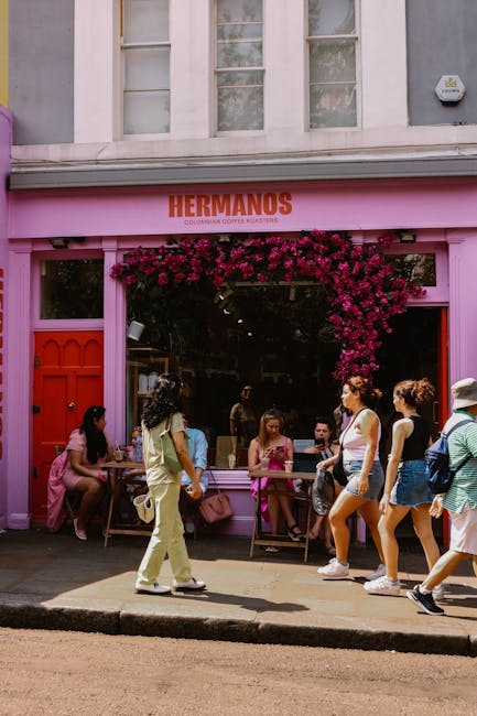 This image captures a vibrant storefront with a pink exterior and a large window adorned with a lush, cascading display of deep pink and magenta flowers, forming a floral arch above the entrance. Outs