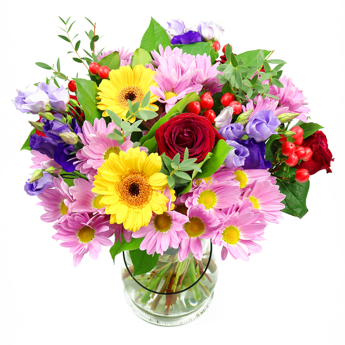 In this image, a vibrant, garden-style bouquet overflows from a clear glass vase, its colours and textures standing out vividly against a plain white background. At the centre, rich red roses unfurl their velvety petals, creating a deep, romantic core that draws the eye. Flanking them are sunny yellow gerbera daisies with striking dark brown-orange centres, their bold, round faces capturing the same cheerful spirit you might feel strolling past the weekend stalls near Portobello Road. Surrounding these central blooms is a generous layer of soft pink and lavender daisies or chrysanthemums, each flower made up of slender petals and tiny yellow centres. These pastel blossoms add volume and a gentle, cosy softness, making the arrangement appear full and welcoming, like a warm greeting at a Notting Hill doorway. Threaded delicately among the daisies and roses, slender stems of purple and lilac lisianthus rise and curve, their bell-shaped, slightly ruffled petals adding an elegant, cool-toned counterpoint to the warmer hues. Between the blooms, shiny red hypericum berries appear in small clusters, their round forms and glossy skins introducing a playful textural contrast, almost like tiny ornaments carefully tucked into the bouquet. Lush greenery in varying shades of green - from broad, deep-toned leaves to lighter, more delicate sprigs - interlaces the flowers, framing the brighter colours and giving the composition a fresh, natural structure. The clear vase reveals neatly cut stems splaying into crystal-clear water, reflecting a careful, professional touch. Altogether, this mixed arrangement feels joyful and expressive, perfect as a centrepiece in a Notting Hill townhouse or as a thoughtful gift to celebrate birthdays, milestones, or simple moments of everyday happiness.